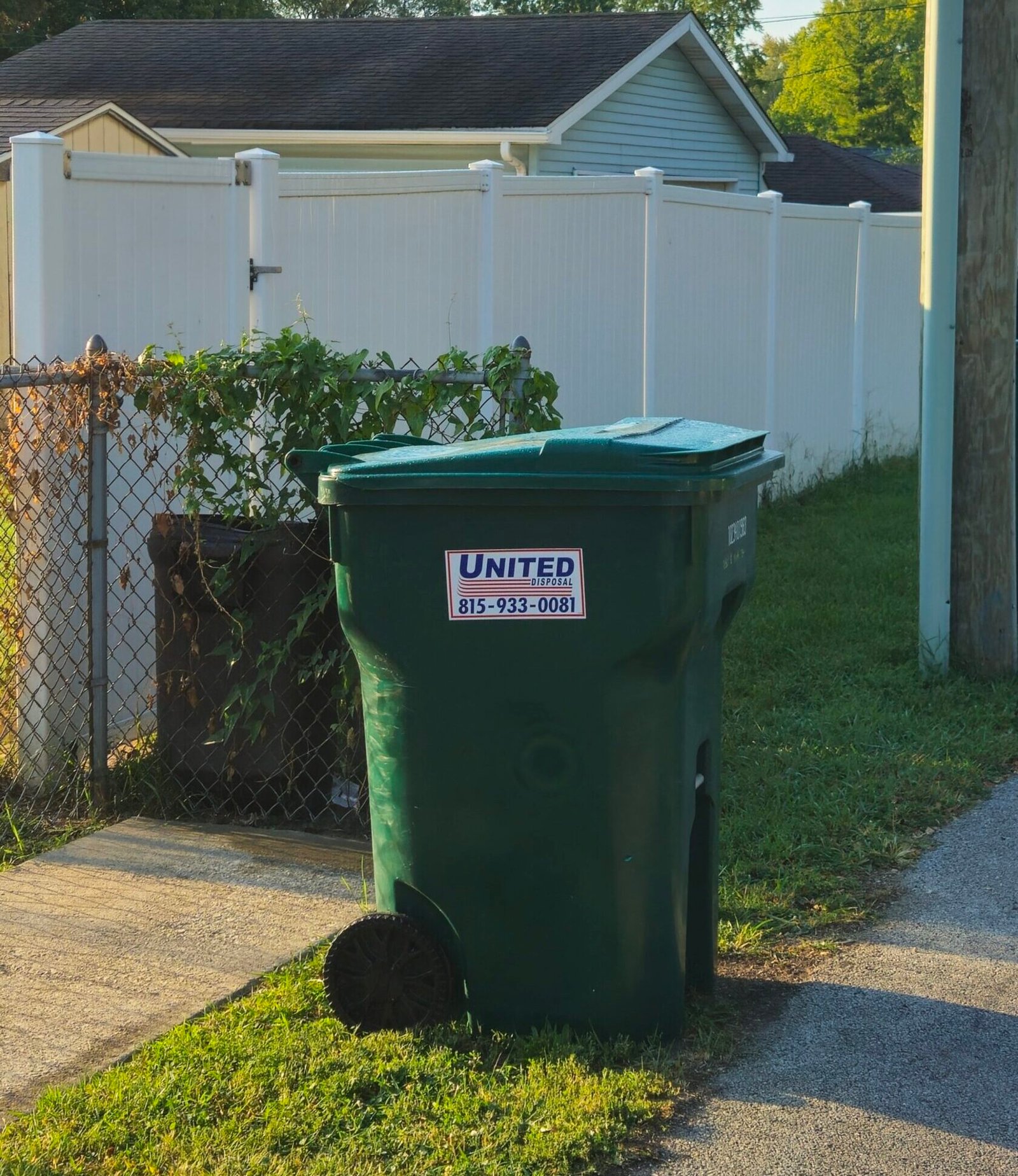 Green United Disposal trash can on a home's lawn. Waste management services.