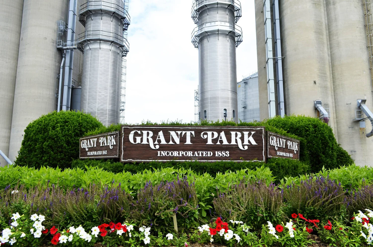 Grant Park service area sign, incorporated 1883. Grain elevators in background. Flowers in foreground.