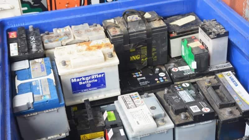 Pile of used car batteries in a blue container. Car battery disposal.