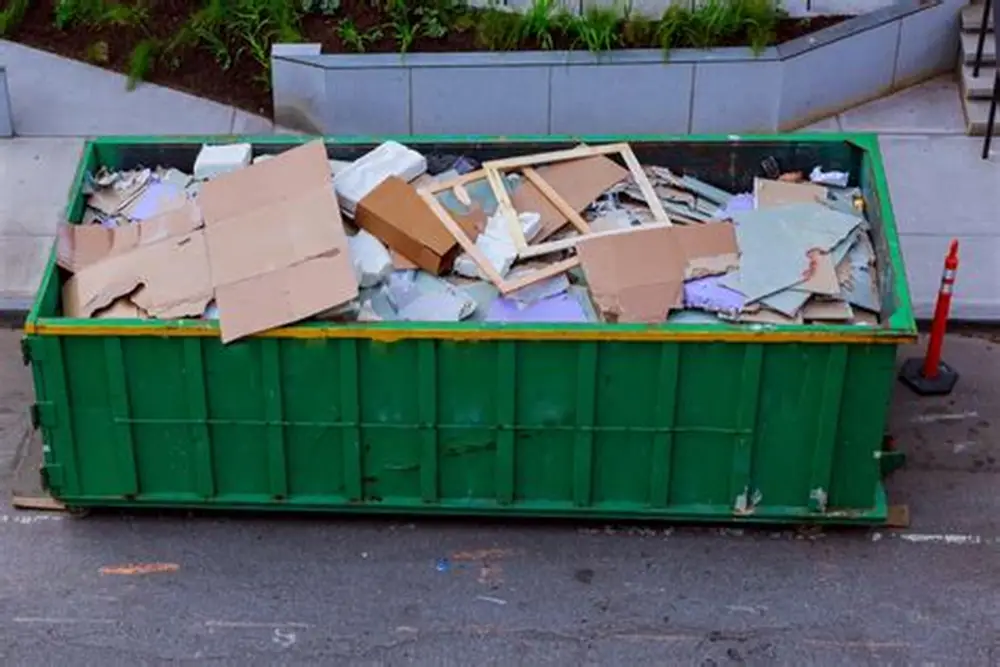 Green dumpster filled with difficult waste. Cardboard, wood, and construction debris. Waste management.