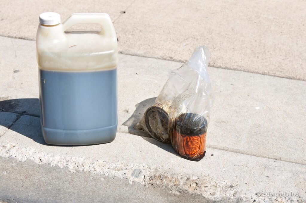Difficult waste: Used motor oil jug and oil filters in plastic bag on concrete. Hazardous waste.