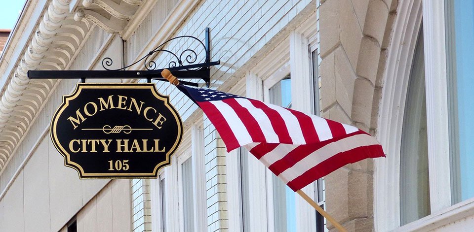 Momence City Hall sign. Service area government building with American flag.