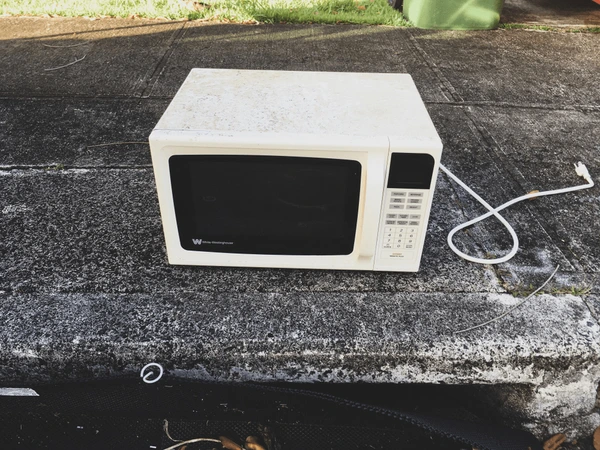 Difficult waste: Old microwave oven on concrete. Appliance disposal.